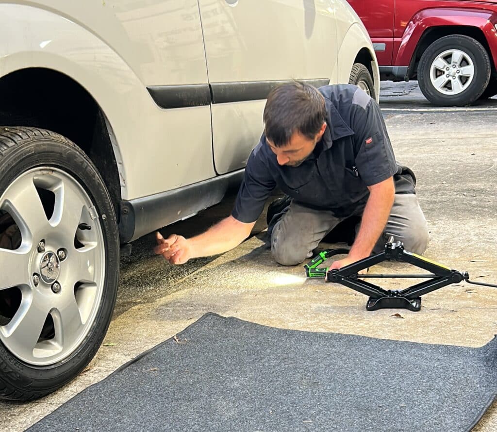 mechanic pointing to the metal location on the underside of a white car where a car should be jacked