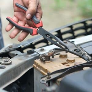 Image of a man working on a car battery with a pair of needle nose pliers.
