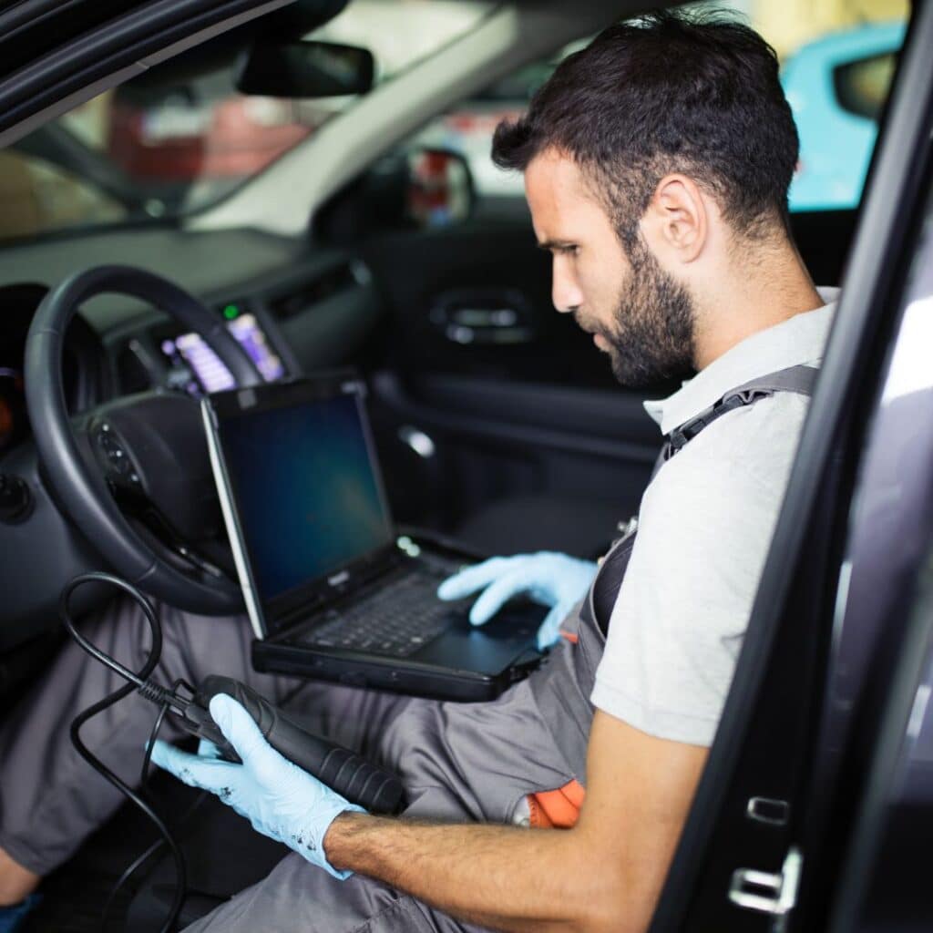 An image of a local mechanic sitting in a vehicle using a diagnostic computer.